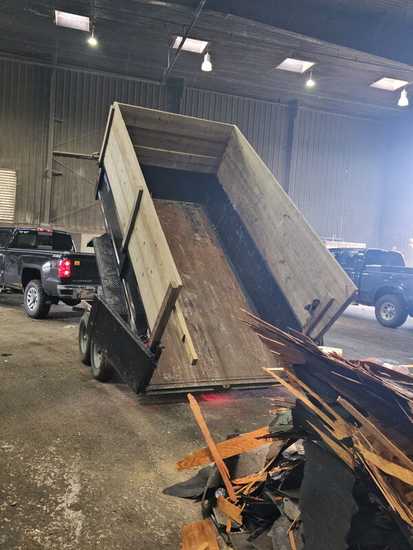 Dump trailer tilted up, emptying a load of roofing shingles and scrap lumber