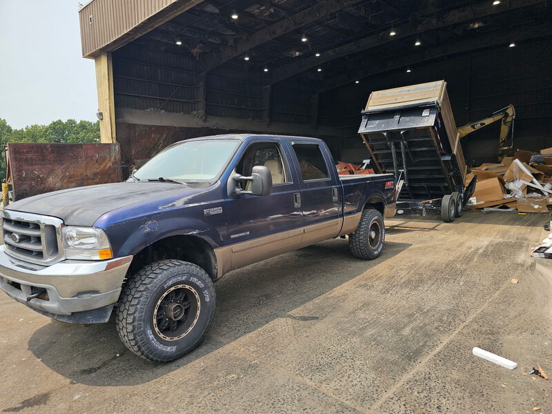 Ford F-250 with the dump trailer raised, unloading construction debris at a transfer station